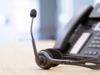 A phone attached to a headset, laying on a desk.